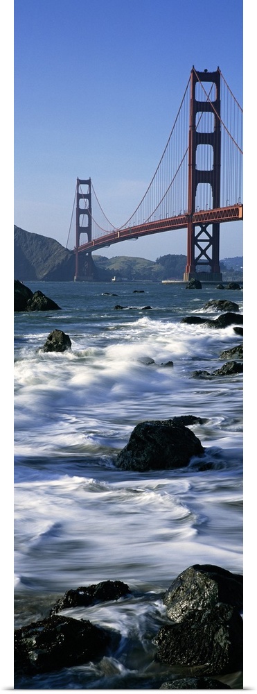 Vertical photograph on a big canvas of the water crashing into the rocks along the shore of Baker Beach, in front of the G...
