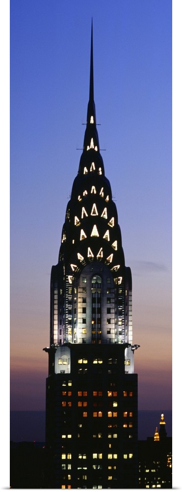 Vertical, oversized photograph of the top of the Chrysler Building in New York City, lit up against the night sky.