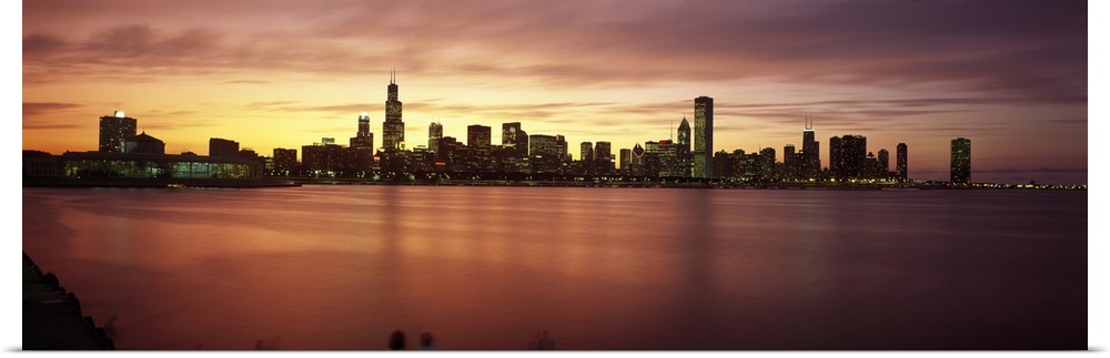 Wide angle, distant photograph of lit skyscrapers of Chicago, over the waters of Lake Michigan, at sunset.