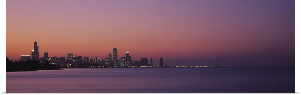 The Chicago skyline is skewed to the left of this panoramic piece and silhouetted by a sunset sky. Lake Michigan largely t...