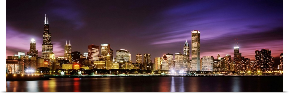 A big cityscape panoramic of downtown Chicagoos lights reflecting off Lake Michigan at night.