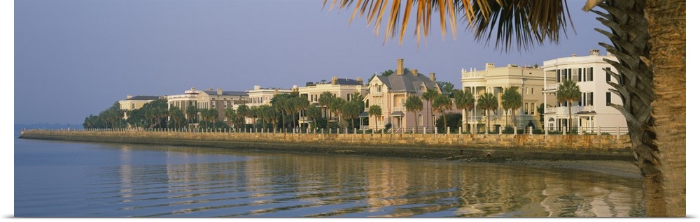A panoramic picture taken of houses on the waterfront in Charleston. Palm trees line the right side of the picture with so...