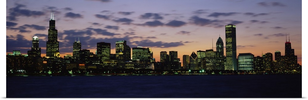 Panoramic photograph shows a skyline on the edge of a river within a lively Midwestern city lit up as the sun begins to set.
