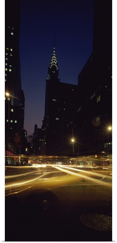 Vertical panoramic photograph of street with light trails lined with lit up buildings in the ""Big Apple.""