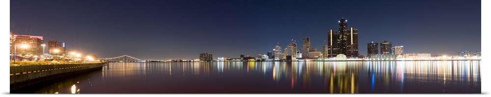 Panoramic image of the Detroit skyline in the evening with the buildings and lights mirrored in the water.