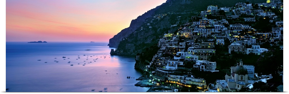 Rustic seaside village densely build up on a cliff side overlooking a harbor reflecting the setting sun.