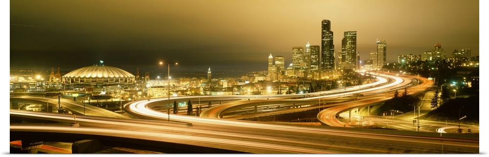 Wide angle, giant panoramic photograph of curving highways leading to a brightly lit skyline in Seattle, Washington.