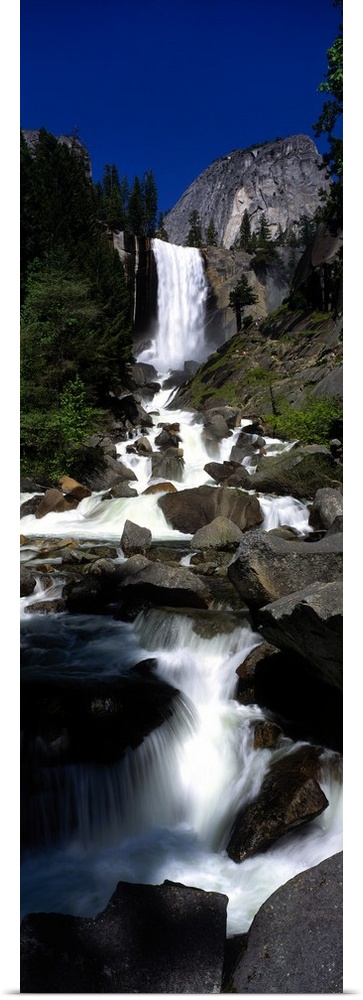 Vertical panoramic photograph of waterfall flowing into a rocky stream surrounded by trees.