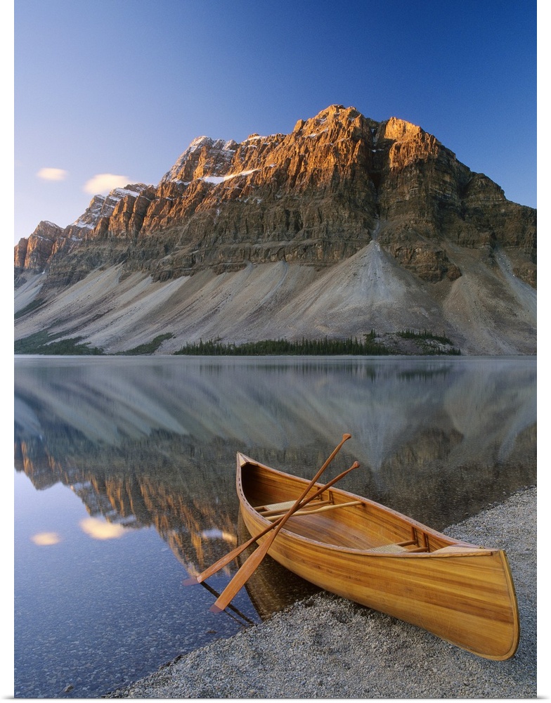 Vertical photograph of a boat on the shore of Bow Lake in Alberta, Canada with a mountain in the background.