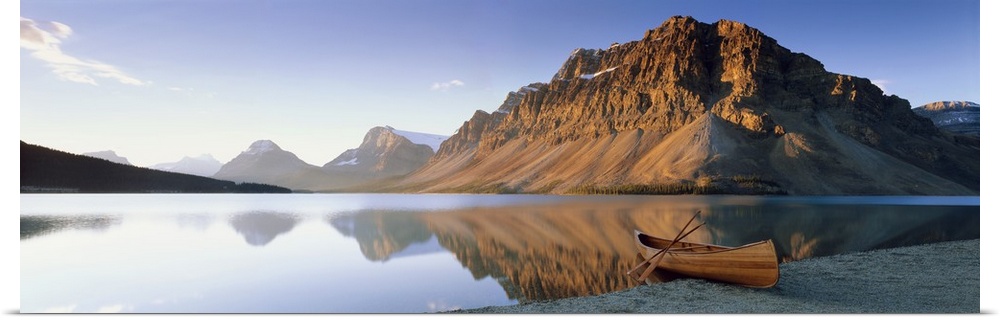 Panoramic photo on canvas of a smooth lake with a wooden canoe on the shoreline and big rocky mountains in the distance.