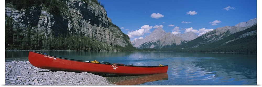 A long canoe is pictured in wide angle view as it sits half in half out of the water. Mountainous terrain lines the side a...