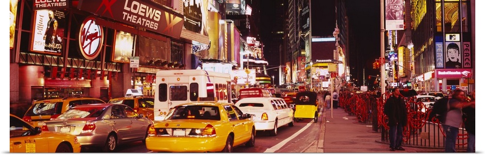Panoramic photograph of many cars and taxis filling the street in Times Square, surrounded by the bright lights and billbo...