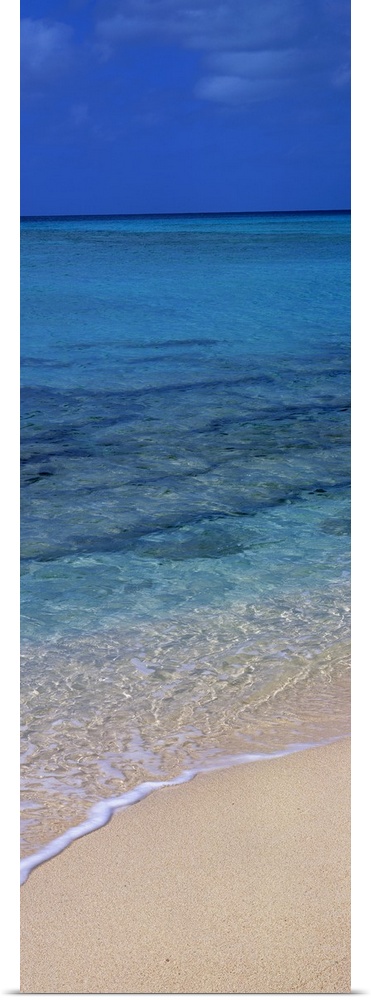 Vertical panorama piece of the crystal clear ocean that is calm as it washes up on the sand.