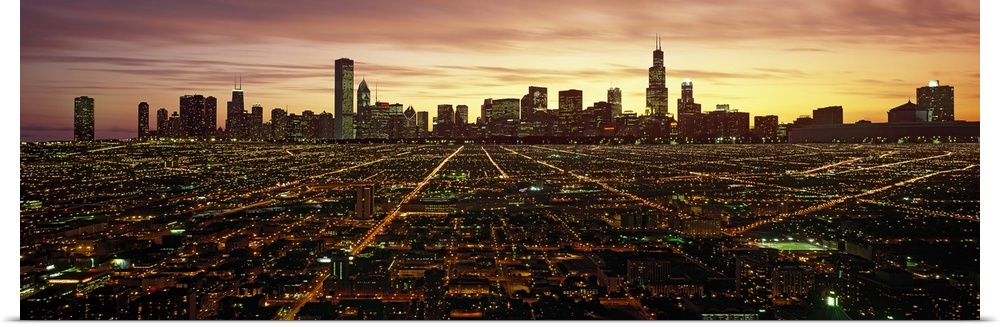 Panoramic photograph of skyline and city lit up at sunset.