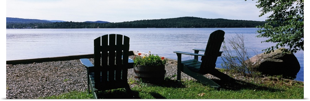 A panoramic photograph of Adirondack chairs arranged with a view of a lake on a bright sunny day.