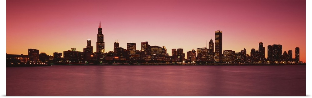 Panoramic photograph of lit up skyline and waterfront at dusk.