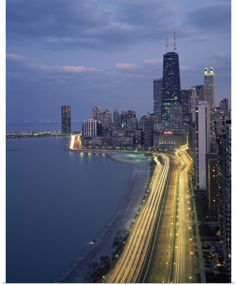Vertical panoramic photograph at dusk with city skyline in the distance and busy highway and streets covered with light tr...