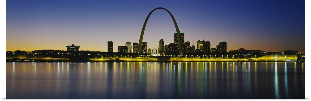 Panoramic photograph of skyline featuring the St. Louis Arch and waterfront at dusk.