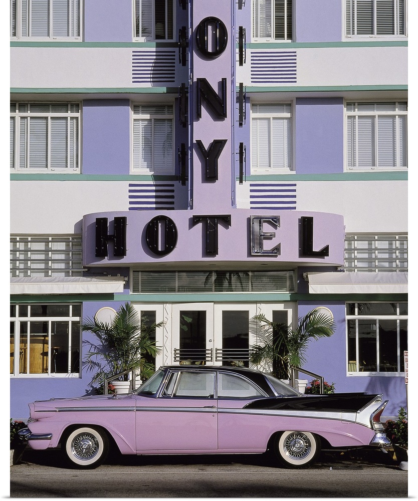 Vertical photograph on a large wall hanging of an old, classic car parked beneath the sign for the Colony Hotel, along Mia...