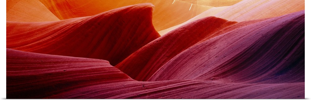 Panoramic photograph of eroded rock in Antelope Canyon, with light forming wavy patters as it bounces of the striations.