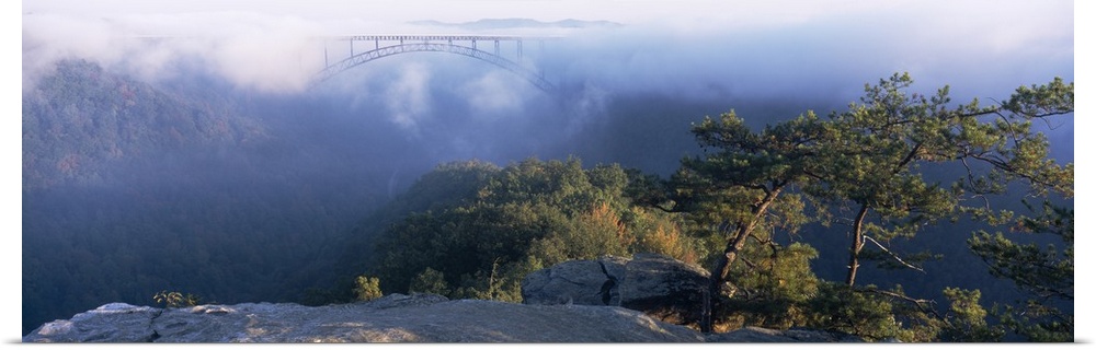 Panoramic image of the new River Gorge Bridge peeking through the fog high above the New River and surrounding Mountains.