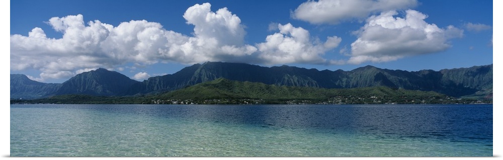 Panoramic photograph taken across the ocean looking at a Hawaiian island with immense clouds floating over.