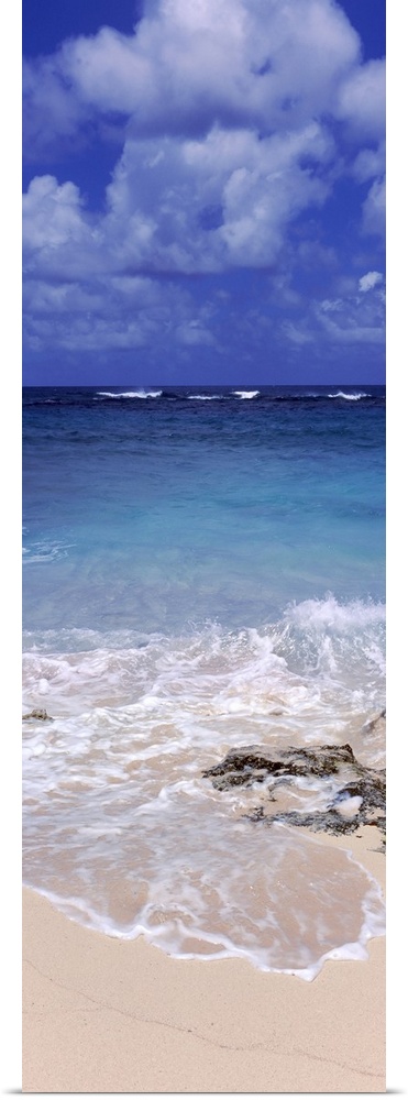 Vertical, large photograph of clear blue waters hitting the beach beneath a blue sky with billowing clouds in Island Harbo...