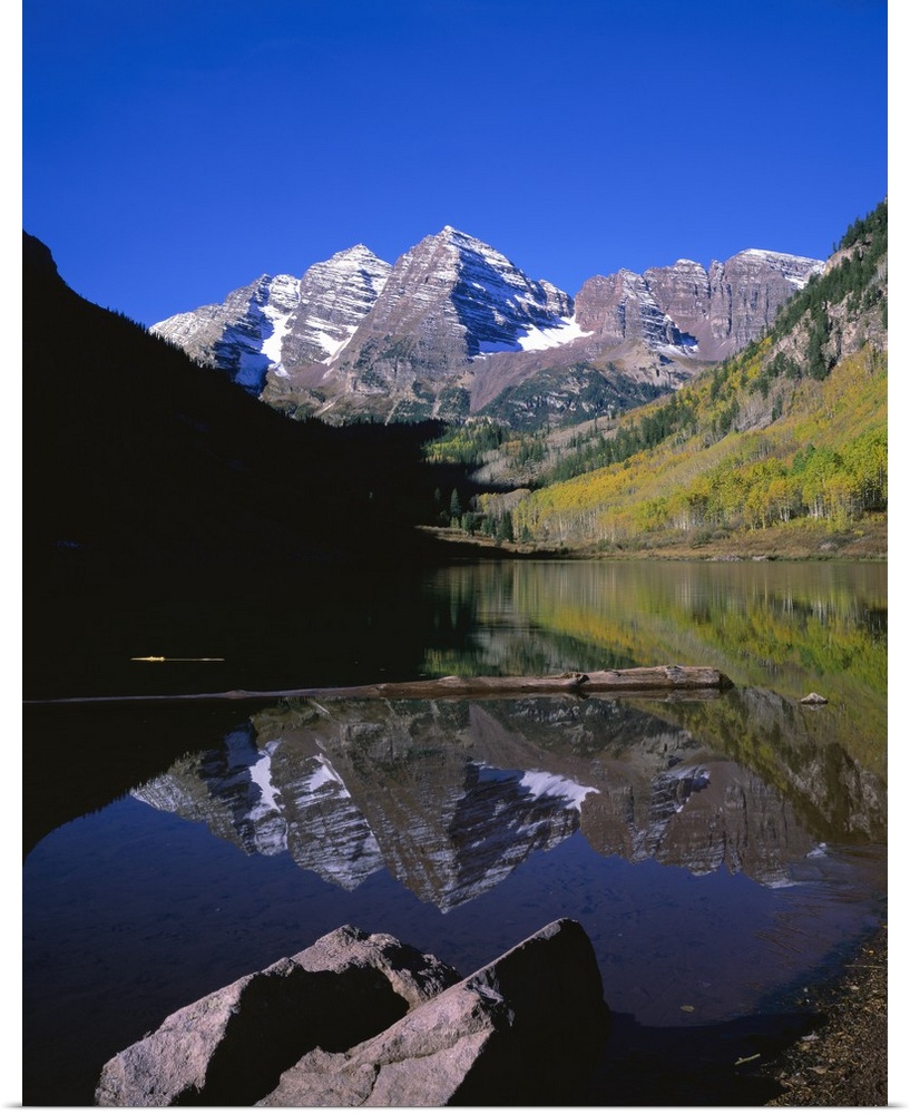 Calm photograph of snowy mountain peaks in the Rocky Mountains, reflected in a still lake of fresh spring water.