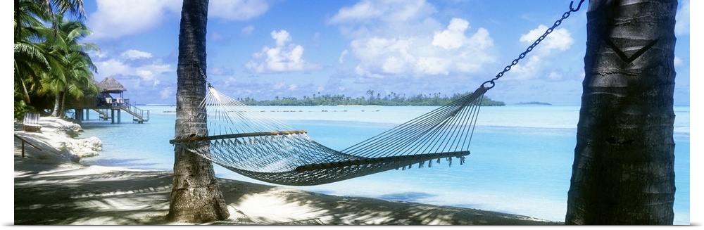Panoramic photograph of a hammock hanging between two palm along the shore of the Cook Islands, clear blue waters of the S...