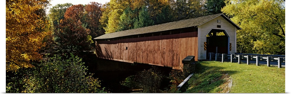Panoramic photograph of the wooden McGees Mill covered bridge, surrounded by a forest of trees with fall foliage, in Clear...