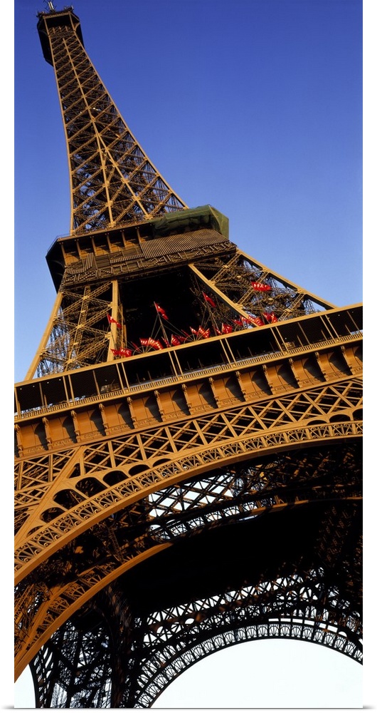 Vertical, close up, low angle photograph of the Eiffel Tower against a blue sky.