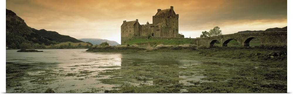 Wide angle photograph taken of a castle in Scotland under a dusk sky with wet land shown in the foreground and hills shown...