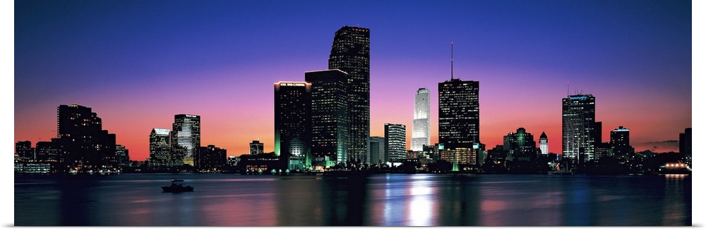 Giant, panoramic photograph of the Miami skyline at night, reflecting over the waters of Biscayne Bay.