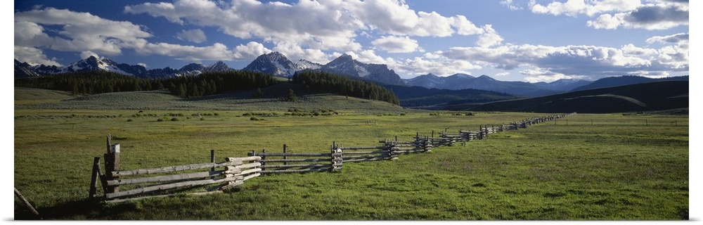 Panoramic picture taken of a vast field with a small wooden fence going as far back as you can see. Mountains line the bac...