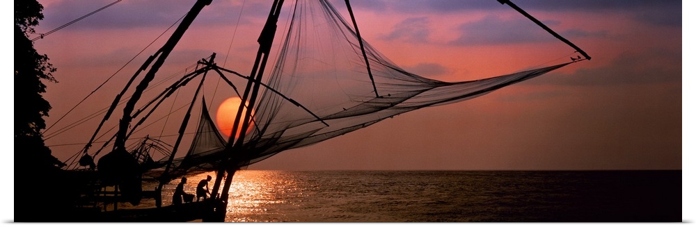 Panoramic photo of fishing nets silhouetted against a big setting sun.