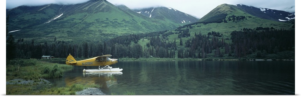 Panoramic photograph of airplane on skis in lake with mountains in the distance.