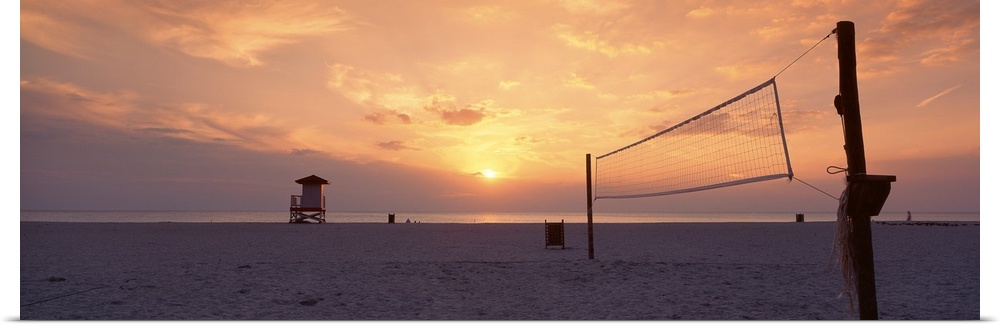The sun sets over a sandy beach which is empty except for a lifeguard tower and a volleyball net.