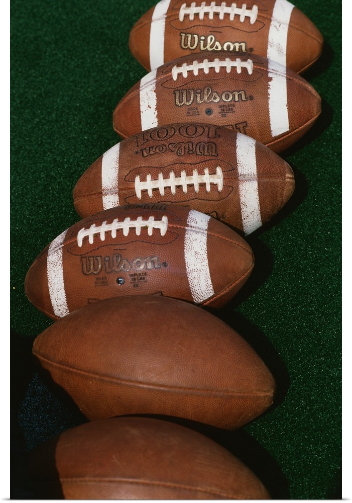 Photograph of six footballs lined up in a row on a field.