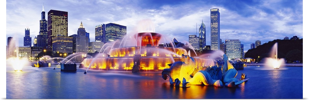 Sculpted mythological beasts spouting water in an illuminated fountain in a city park at twilight.