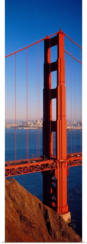 Tall panoramic photo of on of the main portions of the Golden Gate Bridge with cars driving across it and the cityscape in...