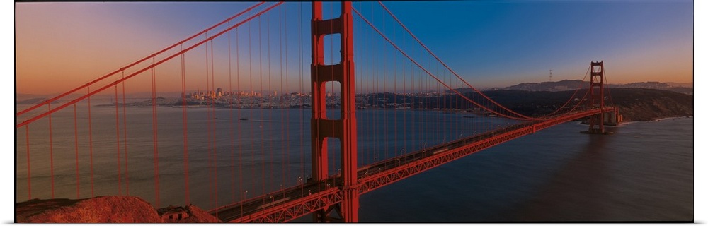 Panoramic photograph of the iconic suspension bridge in California's Bay Area during sunset, with the city in the distance.