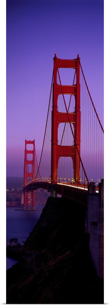 Oversized, vertical photograph taken at an angle of the Golden Gate Bridge at dusk, in San Francisco, California.