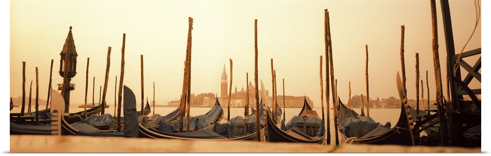 A line of gondola boats are photographed in panoramic view as they sit docked in the water.