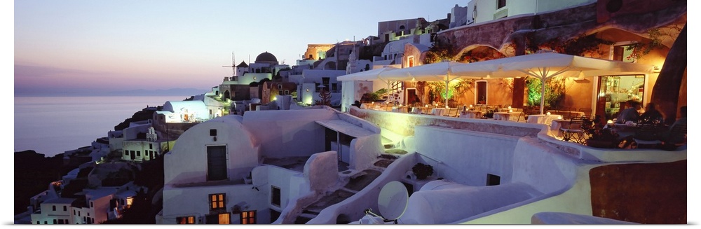 Beautiful white faoade buildings sit on a hill overlooking the Mediterranean Ocean in Santorini, Greece as the pastel sky ...