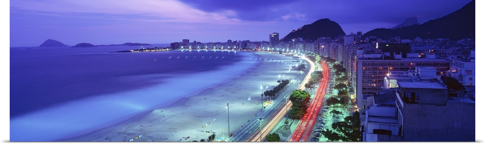 Grand panoramic of Copacabana Beach in Rio de Janeiro at dusk as the cars go speeding by on the beach front road.