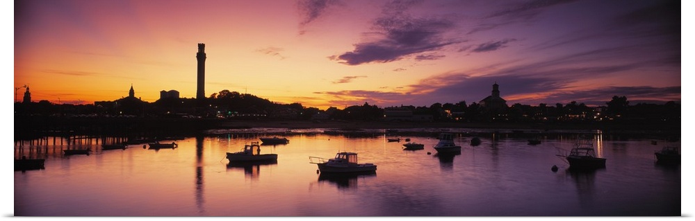 Oversized photograph of the sun setting on the horizon as many boats in a harbor are silhouetted in Cape Cod, Massachusetts.