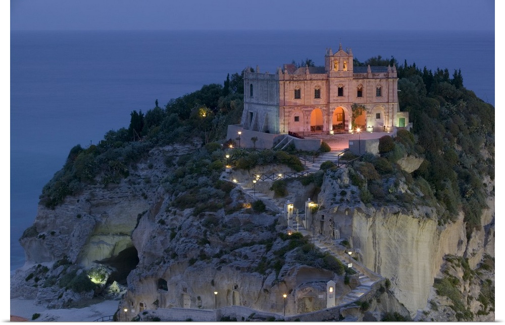 A large church sits on a huge cliff and is illuminated under an evening sky.