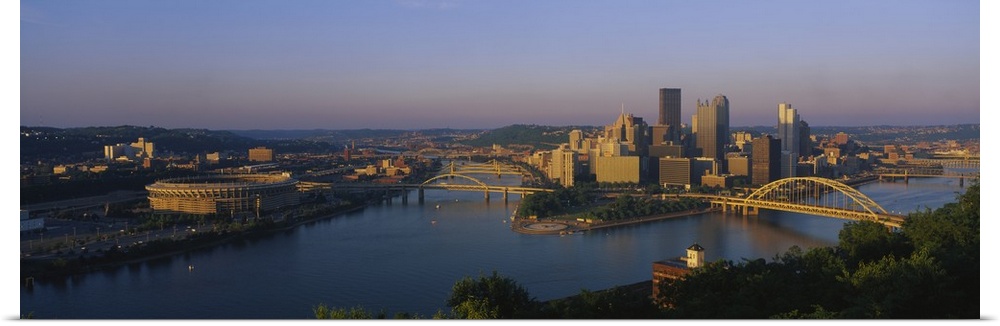 Panoramic photo of the Pittsburgh skyline bathed in morning light, showing skyscrapers and two bridges over the Allegheny ...