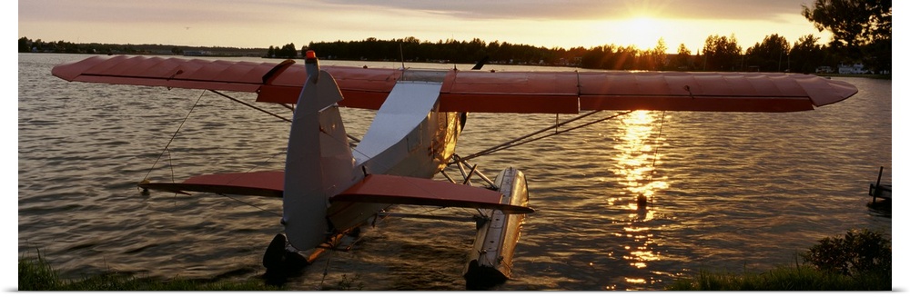 Panoramic photograph of plane sitting in water with forest in the distance at sunset.