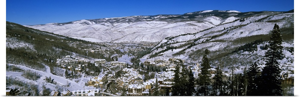 An aerial photograph taken of ski resort planted in the middle of large mountains covered with snow and pine trees.